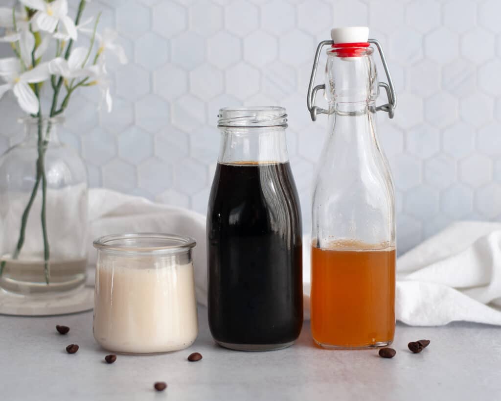 Ingredient shot showing what is needed to make this honey almondmilk cold brew coffee. This includes jars of honey simple syrup, cold brew coffee, and unsweetened almond milk.
