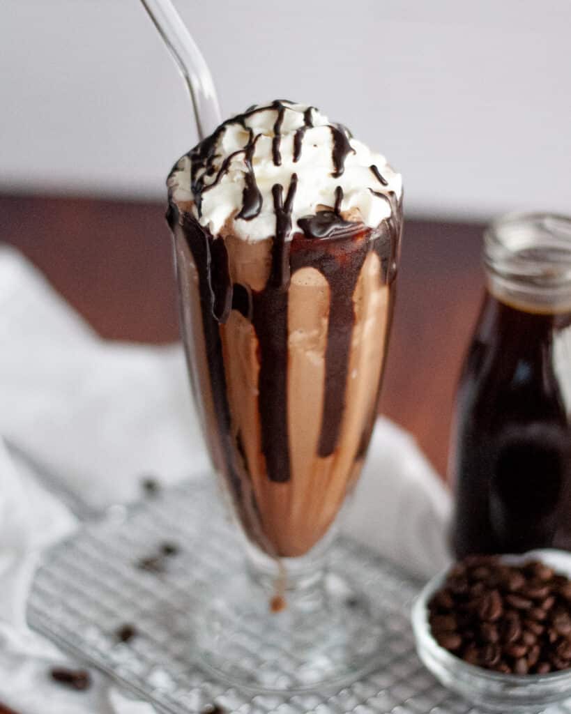 close up of a chocolate coffee milk shake. the coffee milk shake is topped with whipped cream and and chocolate syrup.