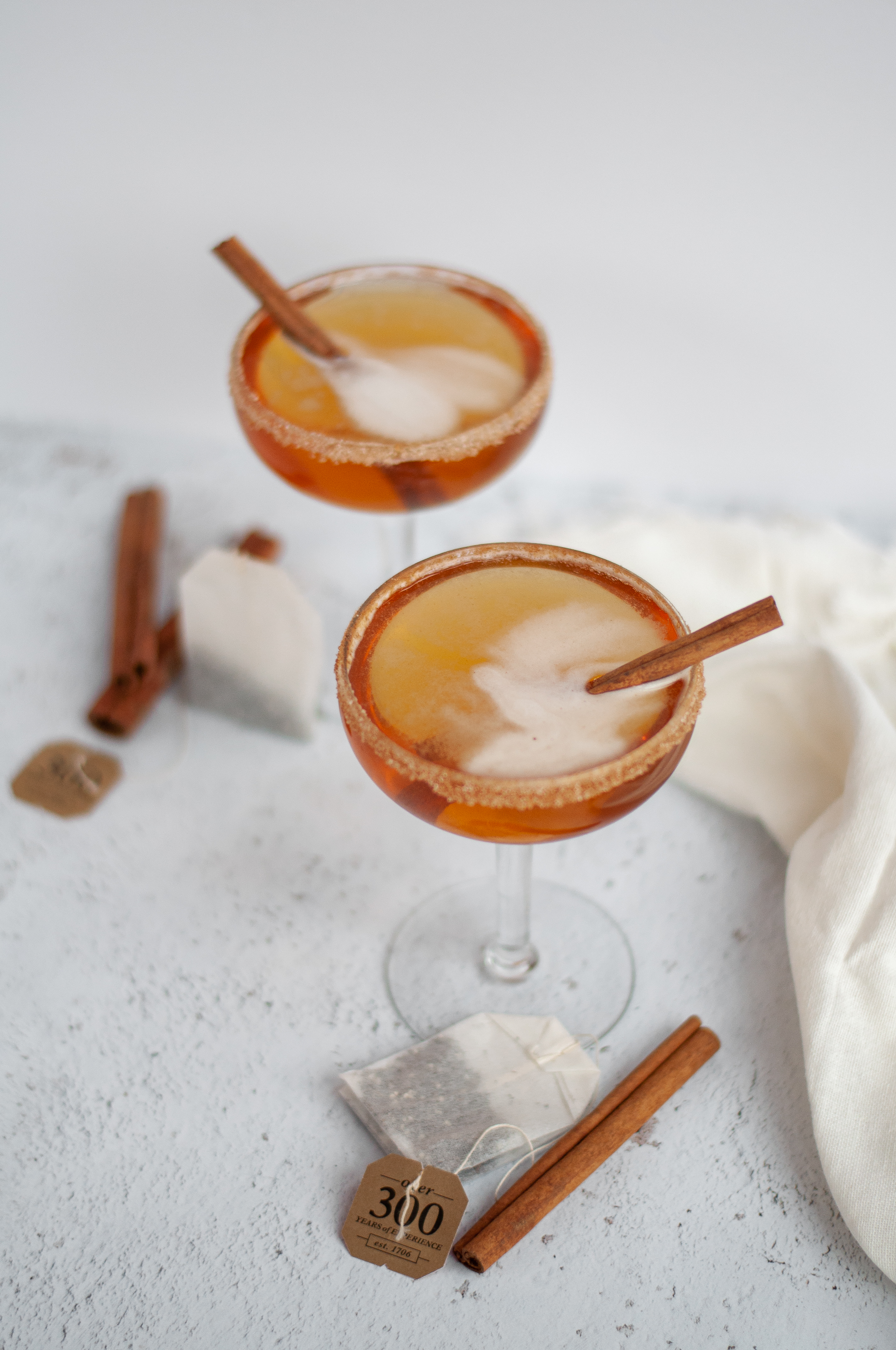 Another view of two coupe glasses filled with this bourbon cocktail recipe, garnished with cinnamon sticks and a cinnamon-sugar rim