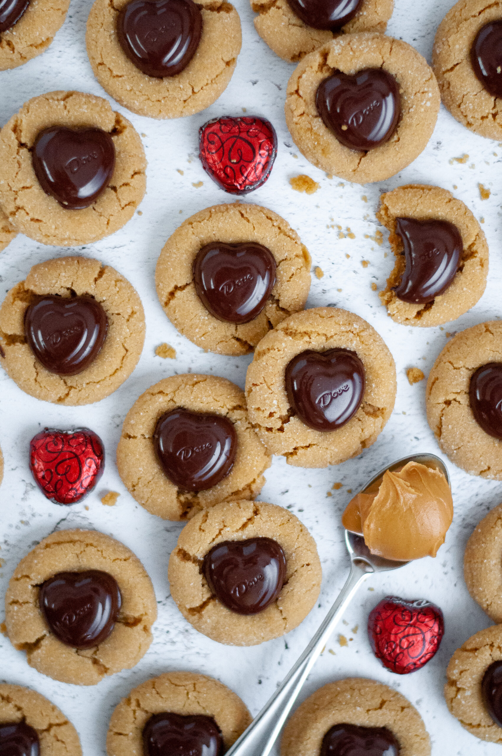 Top down view of these peanut butter blossom cookies with cookie crumbs, a spoonful of peanut butter, and extra heart-shaped chocolates