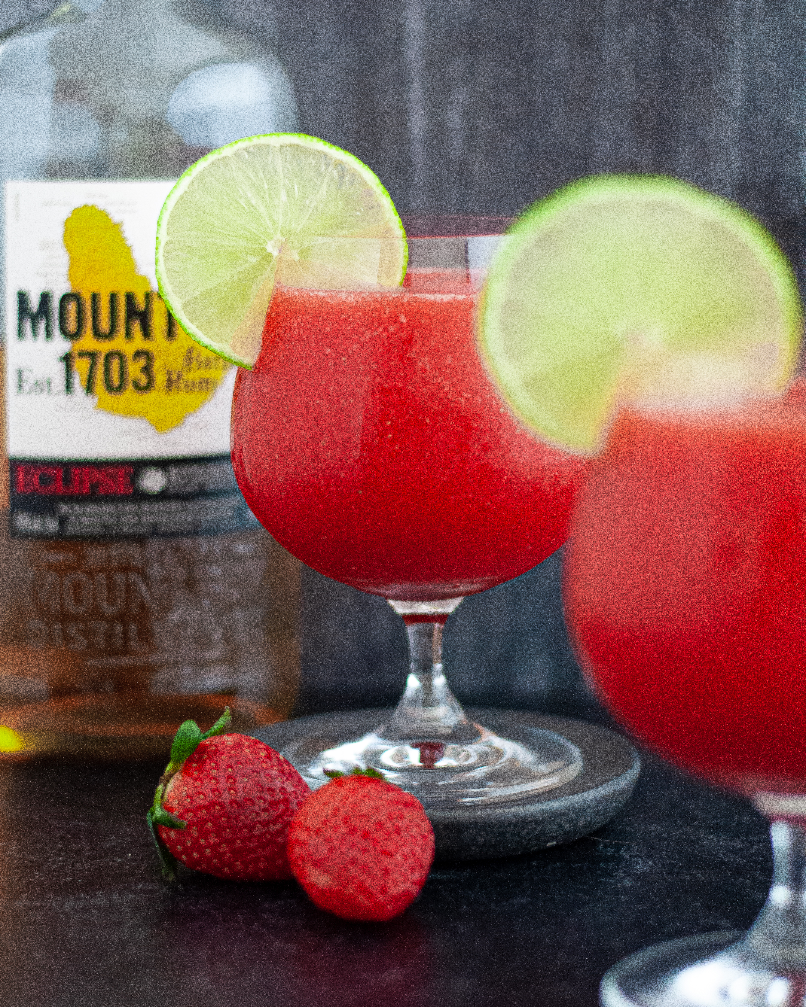 Two glasses of this Frozen Strawberry Daiquiri Recipe served with slices of lime, showcasing the daiquiri ingredients of rum, strawberries, and limes.