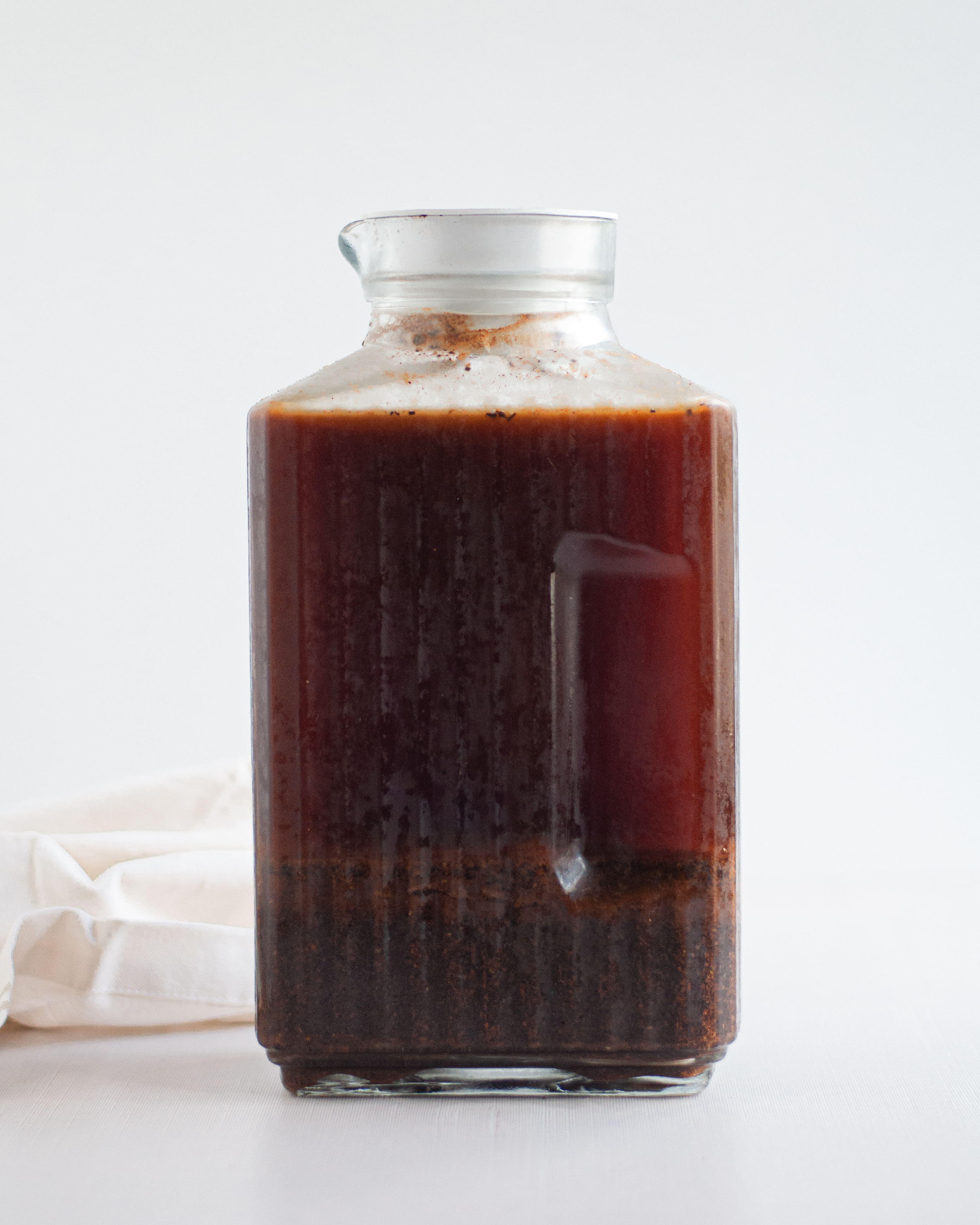 Homemade cold brew concentrate being brewed in a large container with a lid; you can see the course ground coffee and liquid separated and ready to be strained