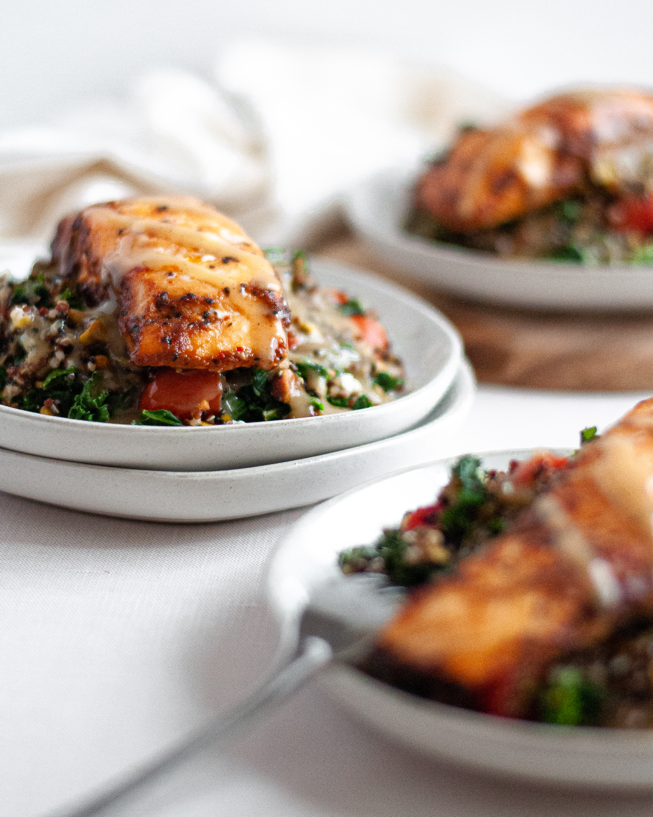 Three servings of kale and quinoa salad, topped with grilled salmon and homemade maple tahini dressing