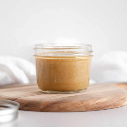 close up of a small jar filled with maple tahini dressing sitting on a wooden board.