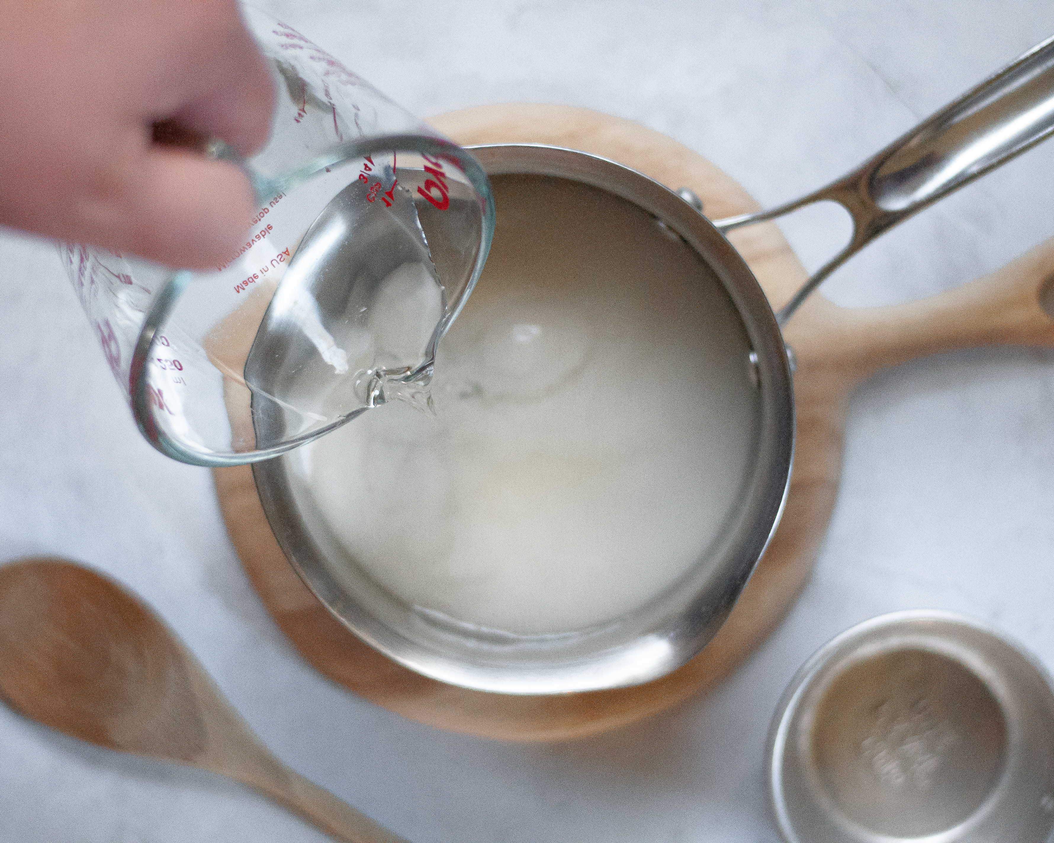 Pouring water into a saucepan with sugar, preparing to make homemade simple syrup.