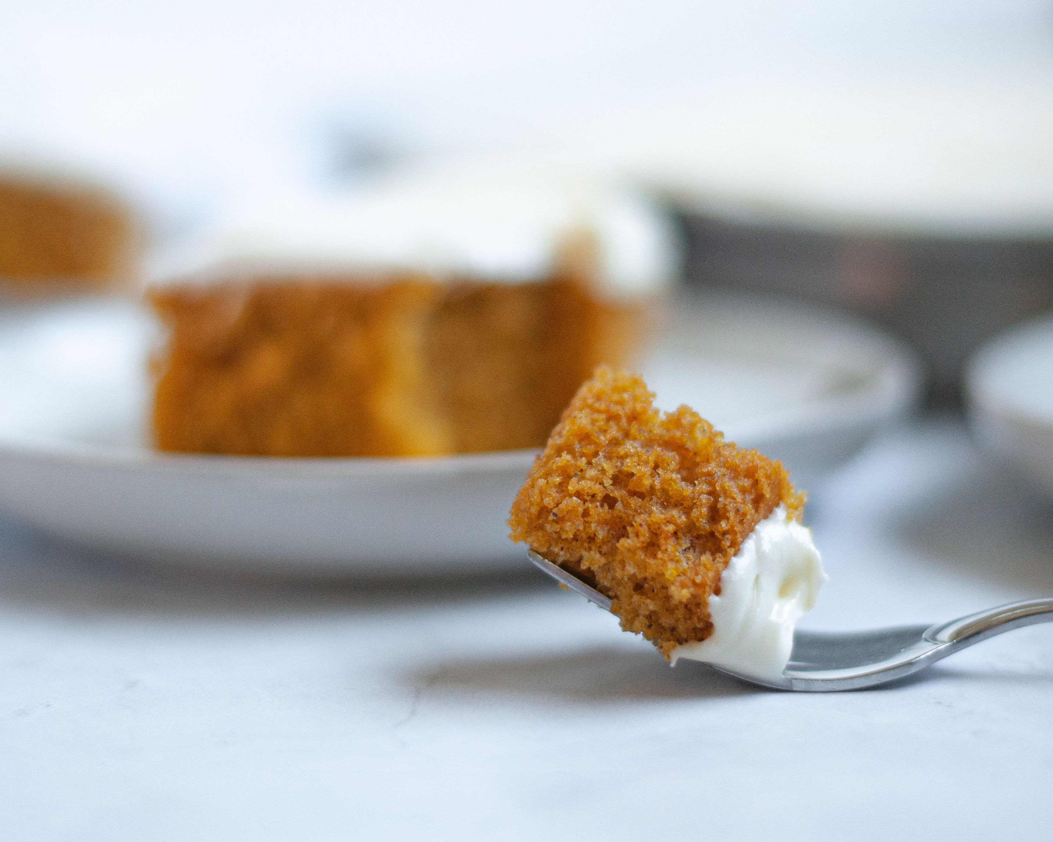 Close up of a fork with a bite of pumpkin bar on it. In the background you can see a plate with a pumpkin square on it