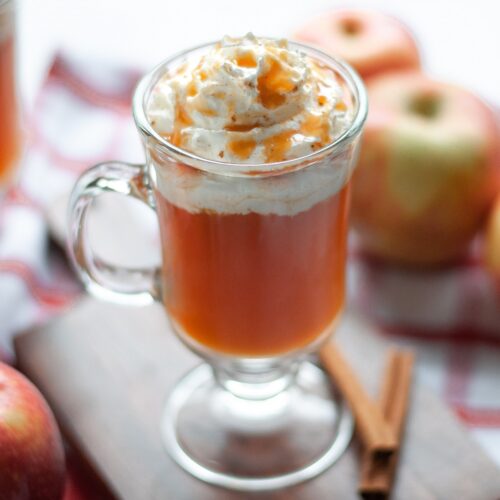 close up of a fancy, glass mug filled high with this starbucks copycat recipe. the Caramel Apple Spice drink is topped with whipped cream and caramel sauce.