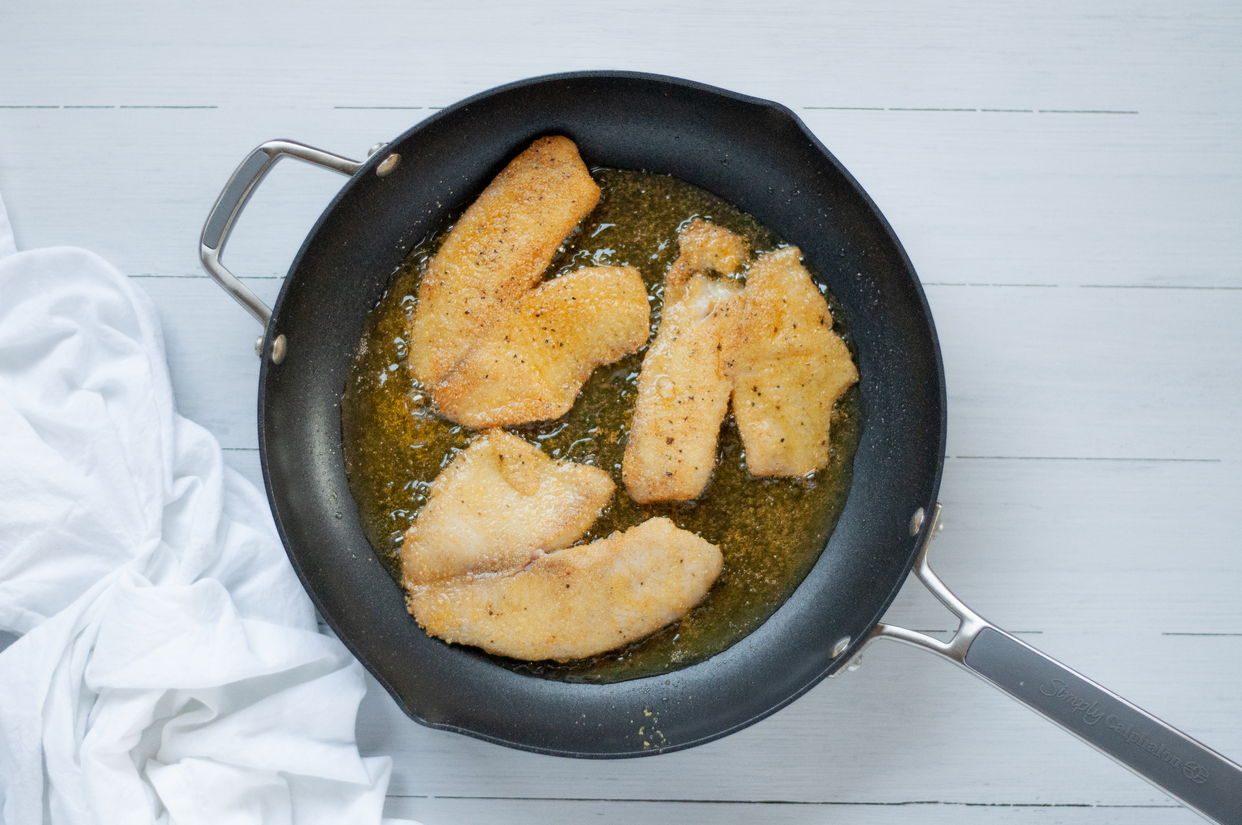 top down shot of three cornmeal crusted tilapia fillets being pan fried