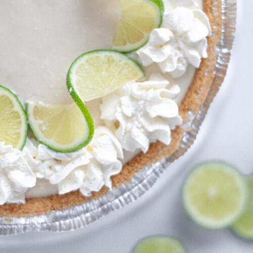 close up view of a freshly made no bake key lime pie decorated with whipped cream and lime slices.