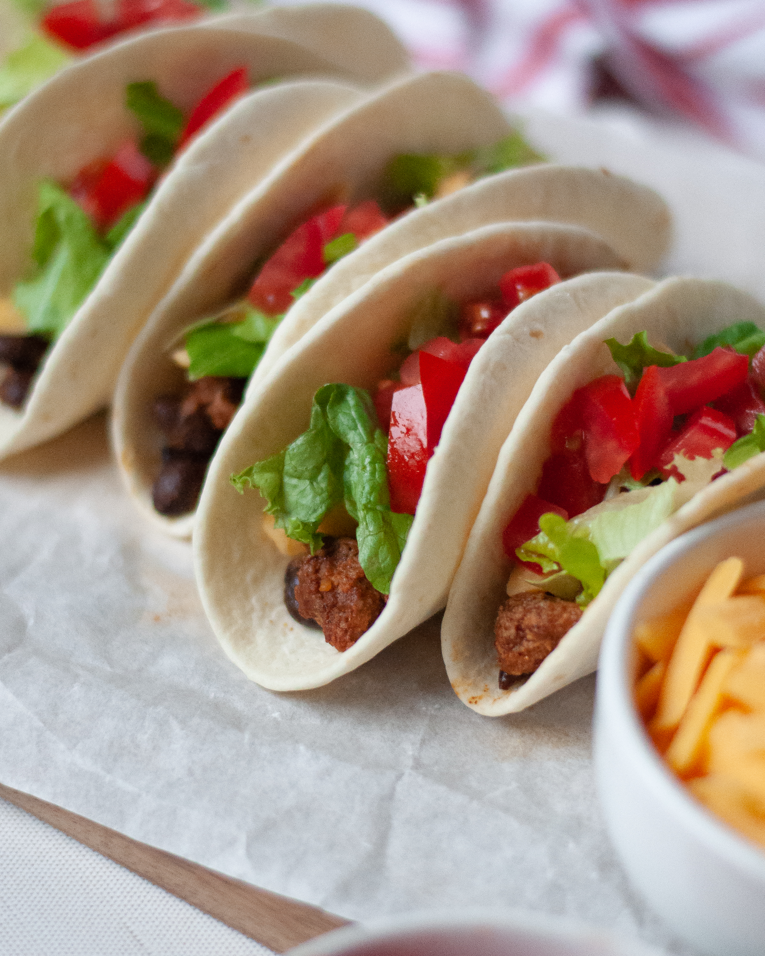 Close up of a tray of turkey tacos with black beans served on tortillas with shredded lettuce, cheese, and tomatoes.