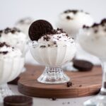 close up of a glass ice cream dish filled with oreo fluff. The main glass that is in focus is surrounded by other glasses of cookies and cream mouse served and ready to eat!