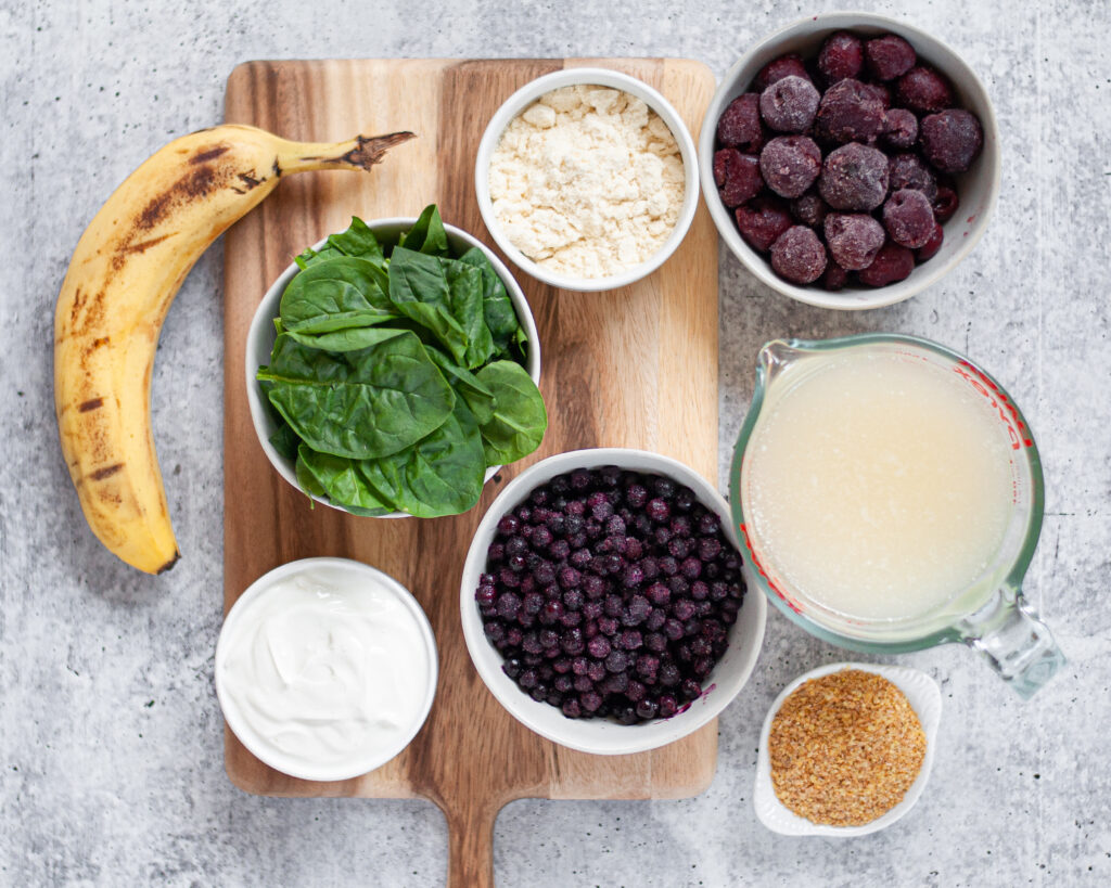 Ingredients needed to make this cherry smoothie recipe. This blueberry protein shake includes a banana, spinach, frozen blueberries, frozen cherries, coconut water, greek yogurt, protein powder, and ground flax.