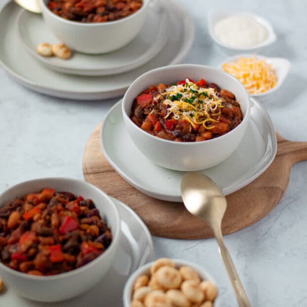 three bowls of vegetarian chili surrounded by crackers, cheese, and sour cream for topping.