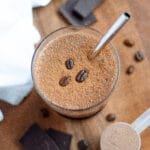 Top-down shot of a chocolate coffee protein shake with three coffee beans and a metal straw within the glass.