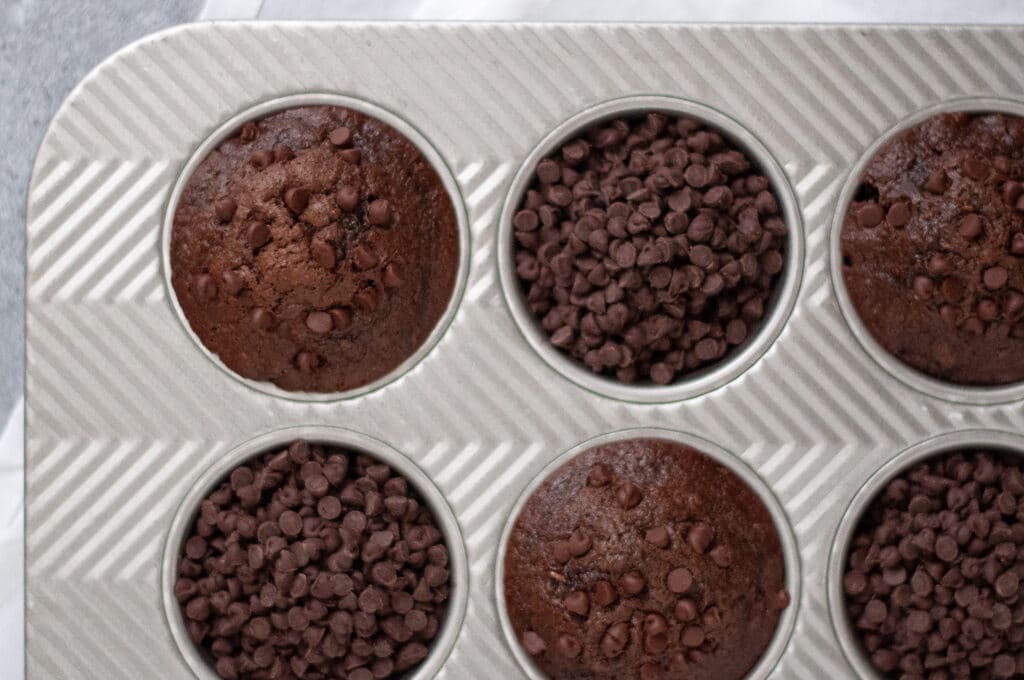 Flatlay of a muffin tin filled with chocolate zucchini muffins and mini chocolate chips (in an alternating pattern)