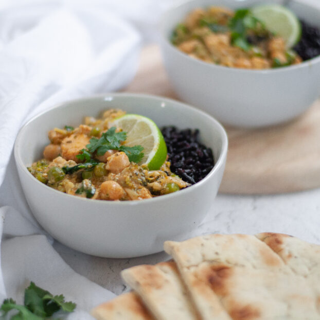 Two bowls of this chicken vegetable curry recipe cooked and served with forbidden rice, a lime wedge, and cilantro. The photo includes naan and a napkin as well.
