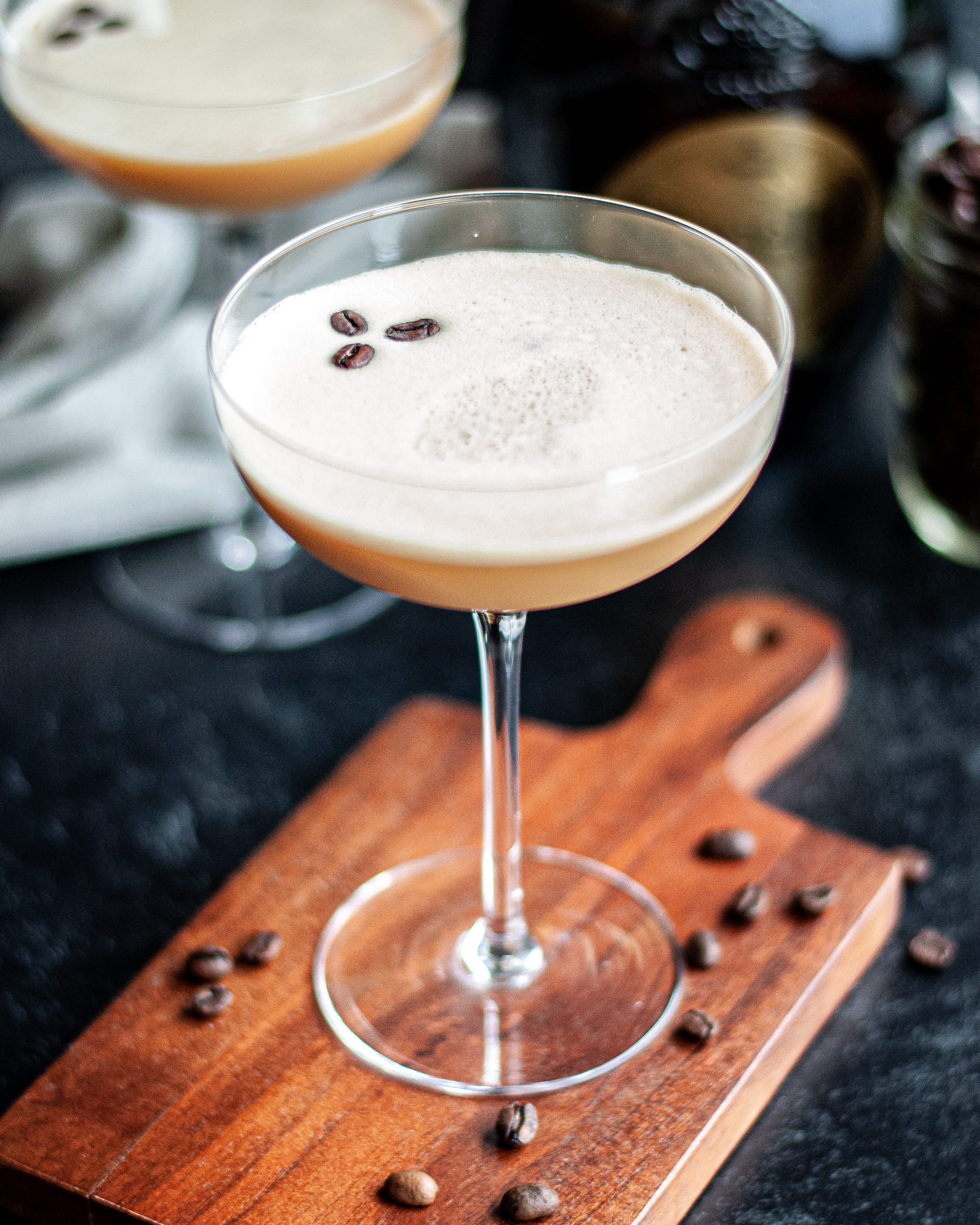 Close up of a coupe glass filled with a frothy cold brew cocktail and garnished with coffee beans.