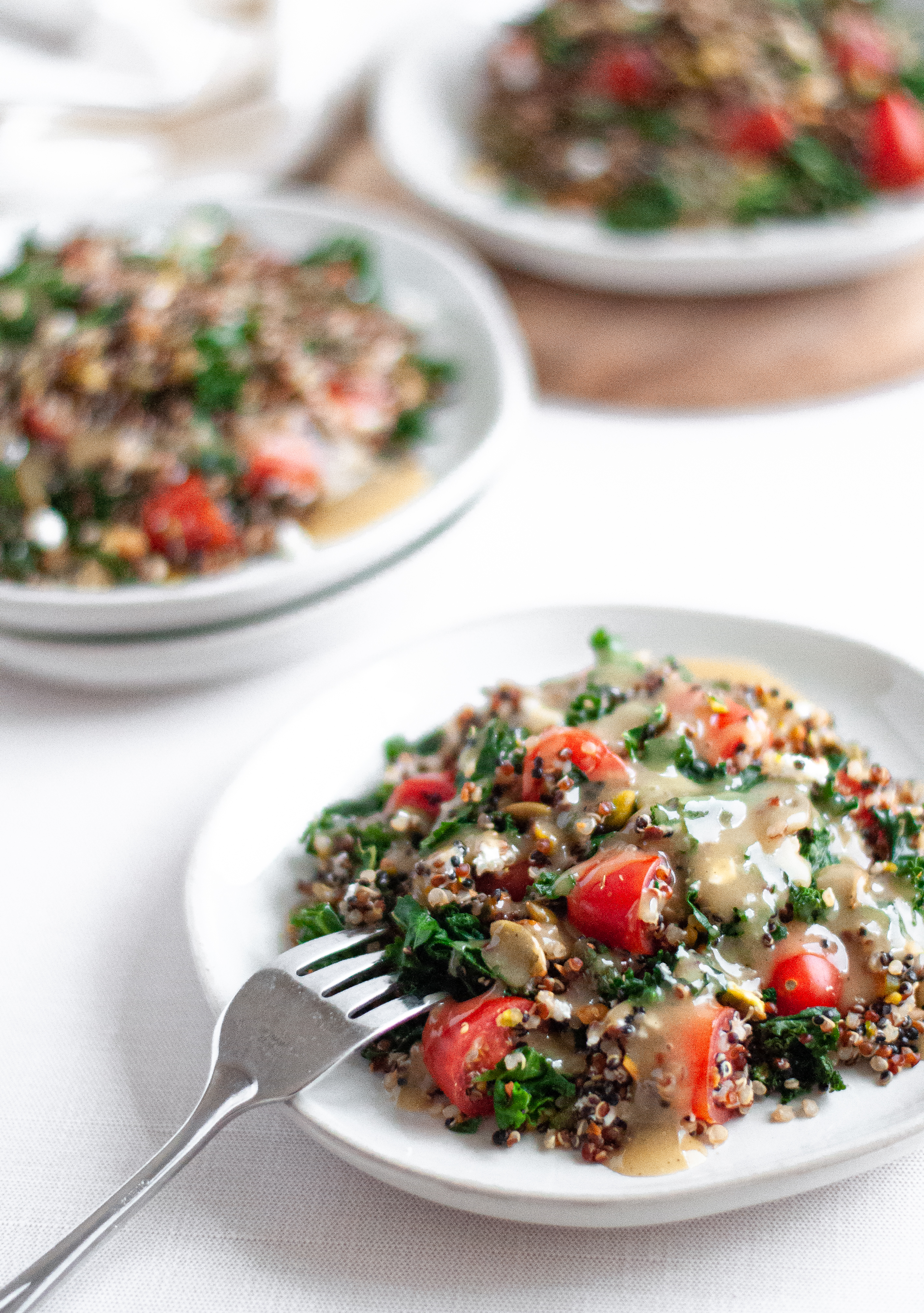 Three plates of kale and quinoa salad, topped with homemade maple tahini dressing