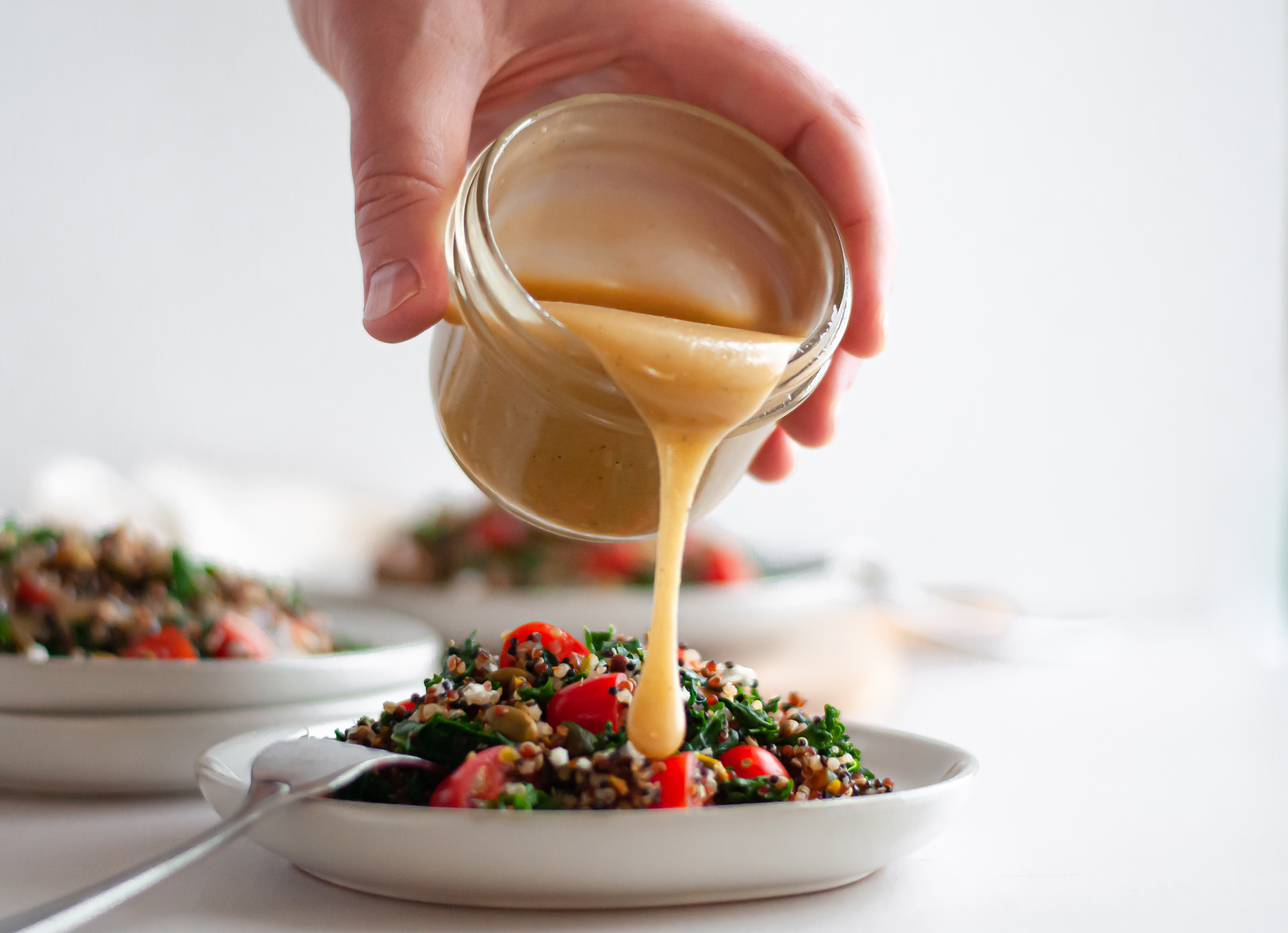 Action shot of hand pouring homemade maple tahini dressing over a kale and quinoa salad