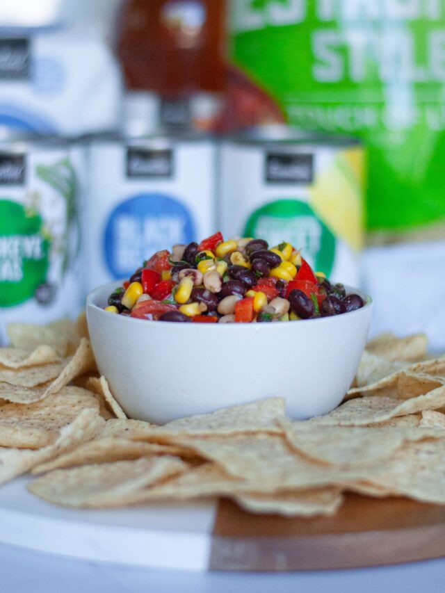 Side-view of a bowl of Texas Caviar salsa with tortilla chips scattered around the bowl.