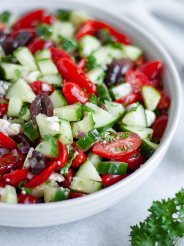 Close-up shot of a Mediterranean Cucumber Salad in a white bowl, with a sprig of parsley beside the bowl.