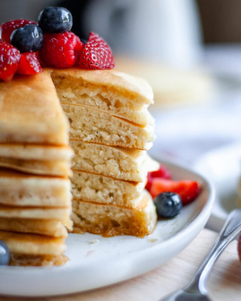 close up for a stack of a stack of oatmilk pancakes topped with berries. You can see the fluffy texture of the pancakes.
