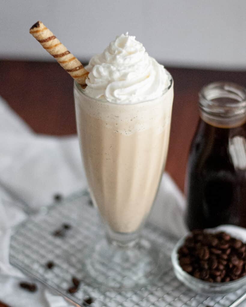 close up of a vanilla coffee milkshake. the coffee milkshake is topped with whipped cream and garnished with a pirouette cookie.