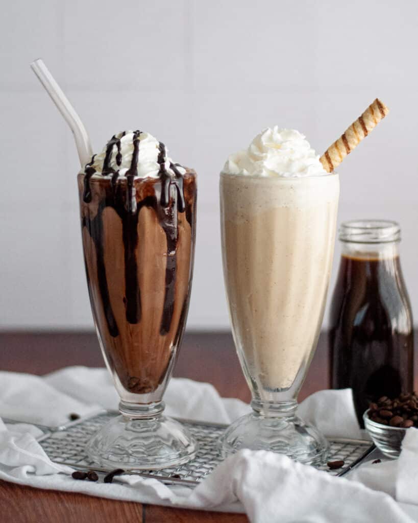 two milkshake glasses filled with coffee milkshakes. the chocolate based coffee malt is on the left and the vanilla coffee milkshake is on the right.