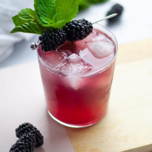 close up of a lowball glass of blackberry whiskey smash garnished with fresh mint and blackberries on a cocktail pick.
