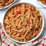 Serving bowl of cajun pasta with plates of pasta around it, and a red and tan linen.