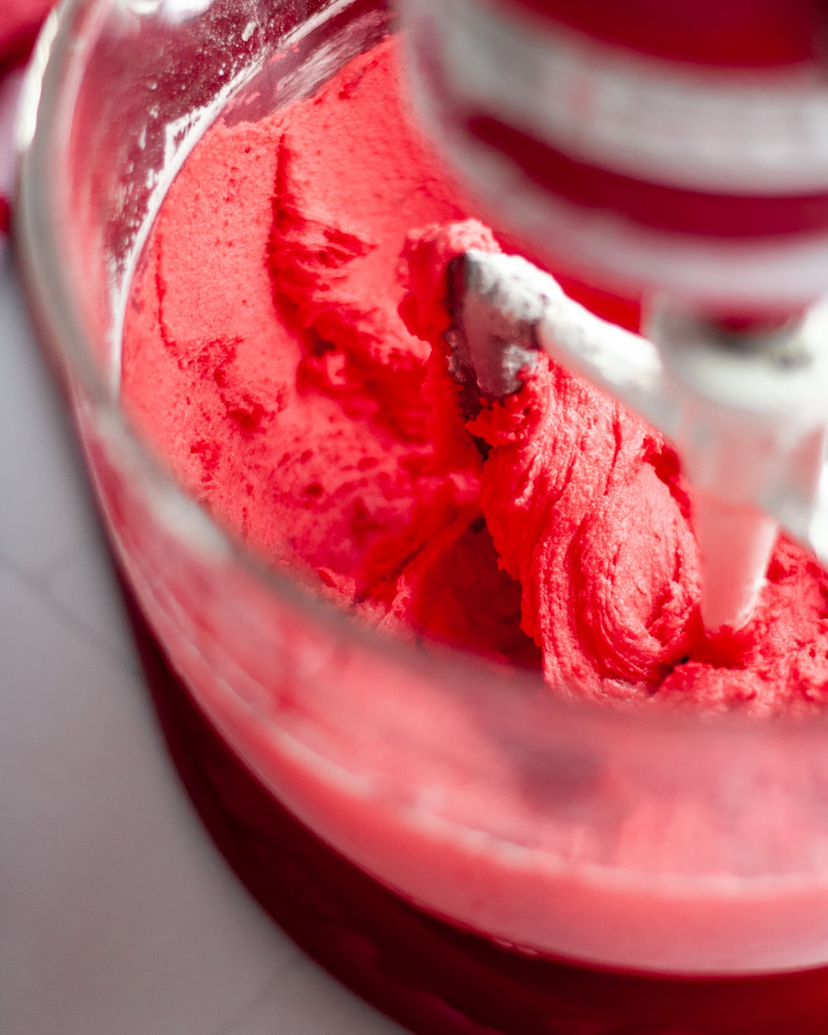 close up of a paddle attachment in a stand mixer mixing the bright red dough together.