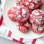 white plate full of red and white chocolate cherry crinkle cookies set on a red and white checkered linen.