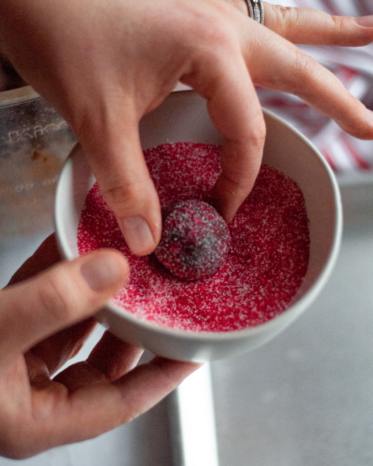 A chocolate dough ball being dipped into the red and white sugar mixture.