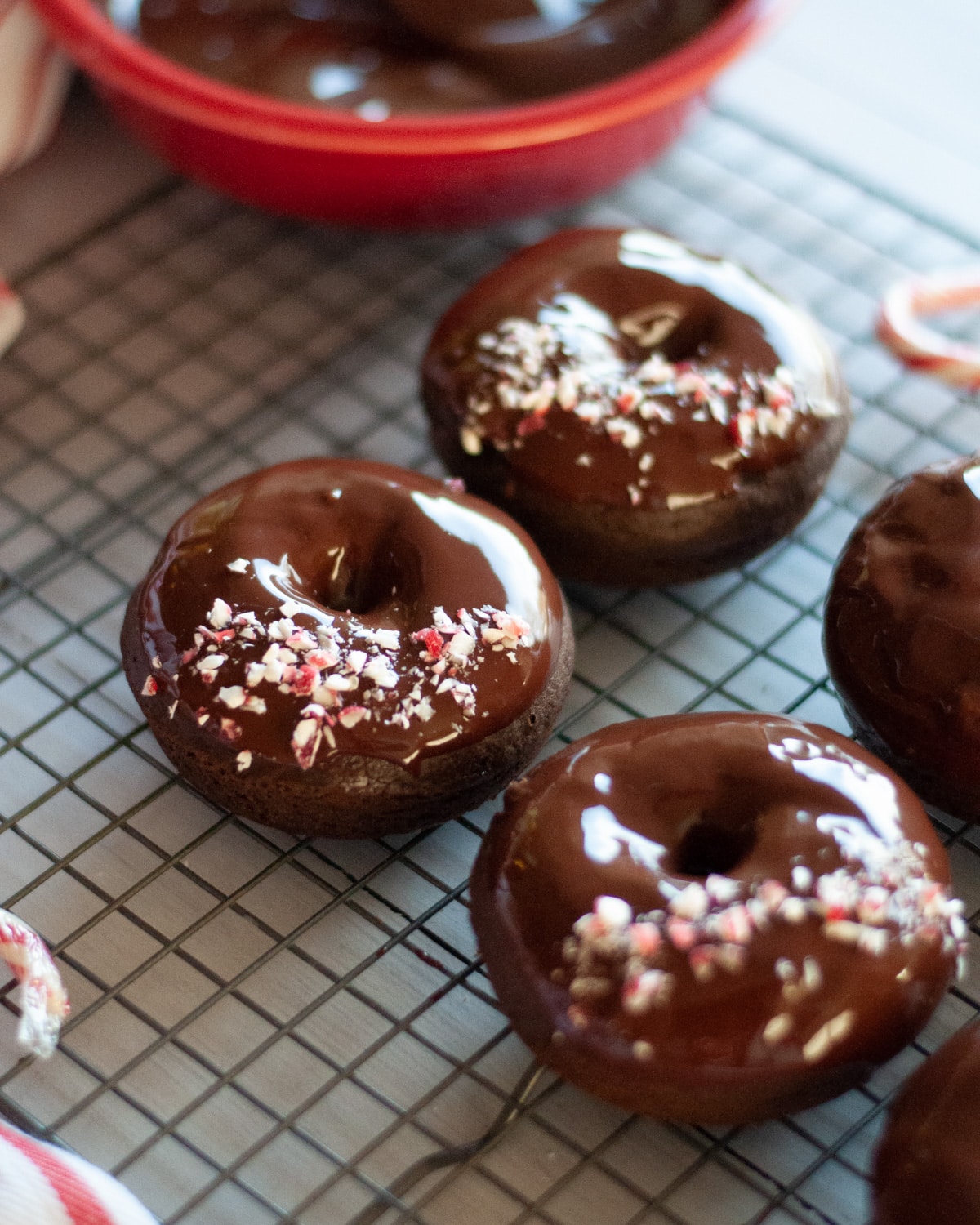a cooling rack full of peppermint mocha donuts freshly dipped into chocolate ganache and topped with a line of crushed candy canes.