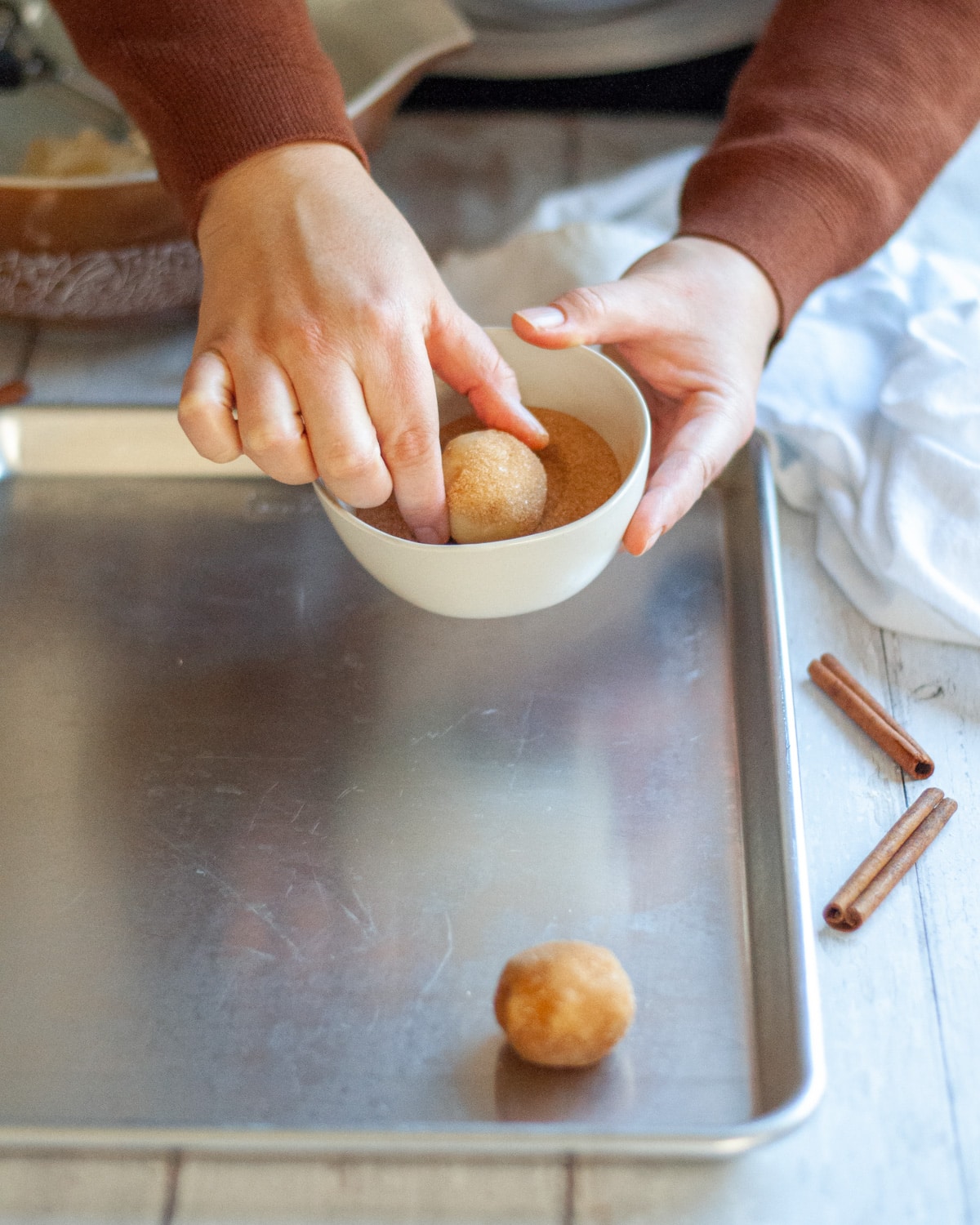 process shot of a rolled ball of dough being dipped into cinnamon-sugar.