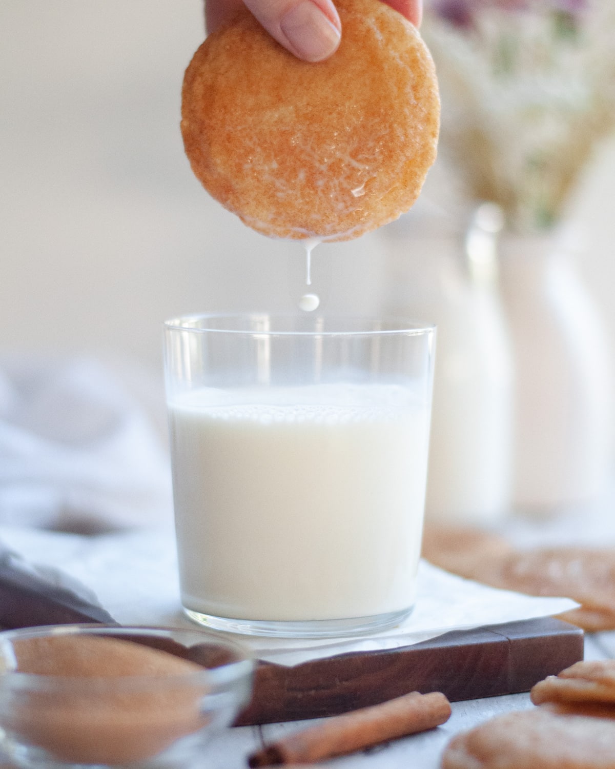 a snickerdoodle just dipped in a glass of milk. a drop of milk is falling off the bottom of it.