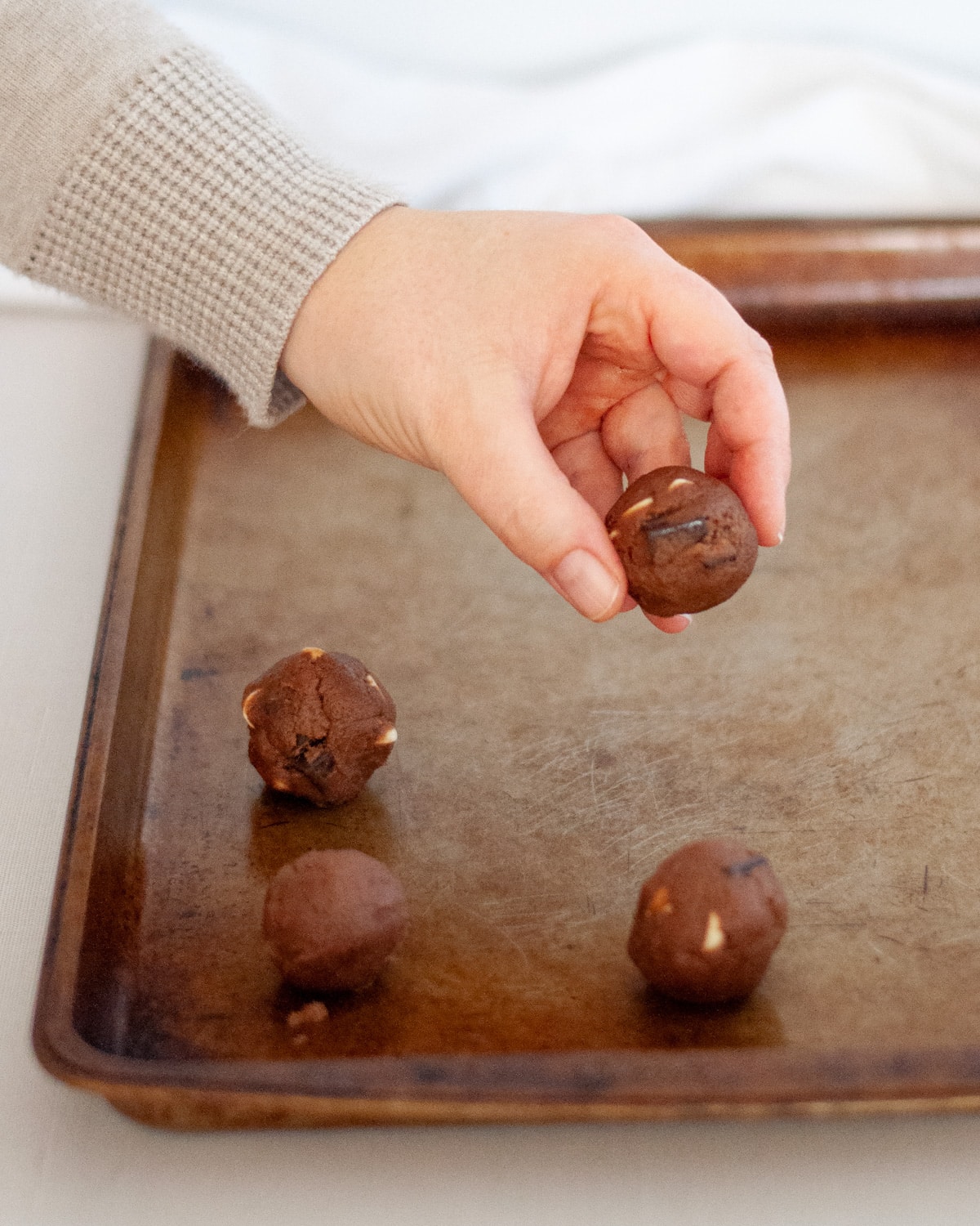 a hand placing a freshly rolled dough ball onto a baking tray.