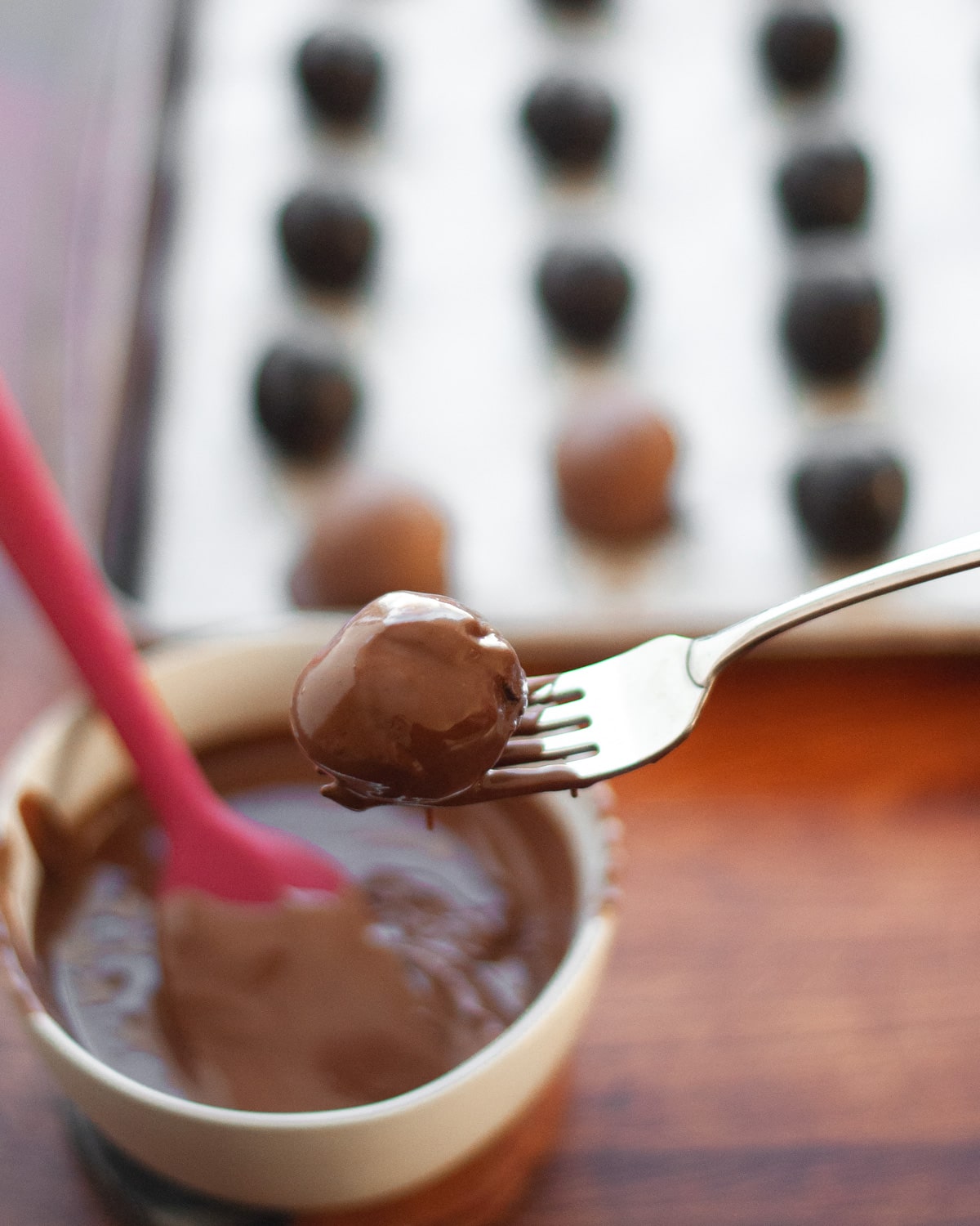 process shot showing how to make oreo balls. showing a chilled ball being dipped in melted chocolate. the ball sits on a fork to let excess chocolate drip off.