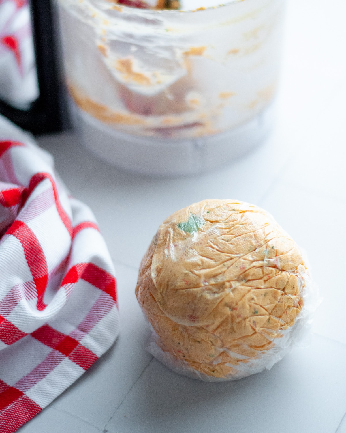 a freshly made cheeseball wrapped in saran wrap ready to be put in the fridge and cooled prior to serving.