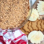 top down view of a glass pie pan filled with homemade caramel apple dip with toffee bits. Next to it is a board covered with gingersnap cookies and fresh apple slices as well as a red and white linen.