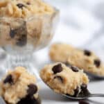 a glass bowl of high protein cookie dough surrounded by spoons full of edible cookie dough.
