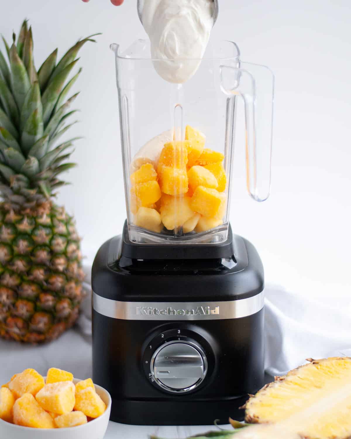 process shot showing how to make a mango pineapple smoothie, showing ingredients being added to a blender.