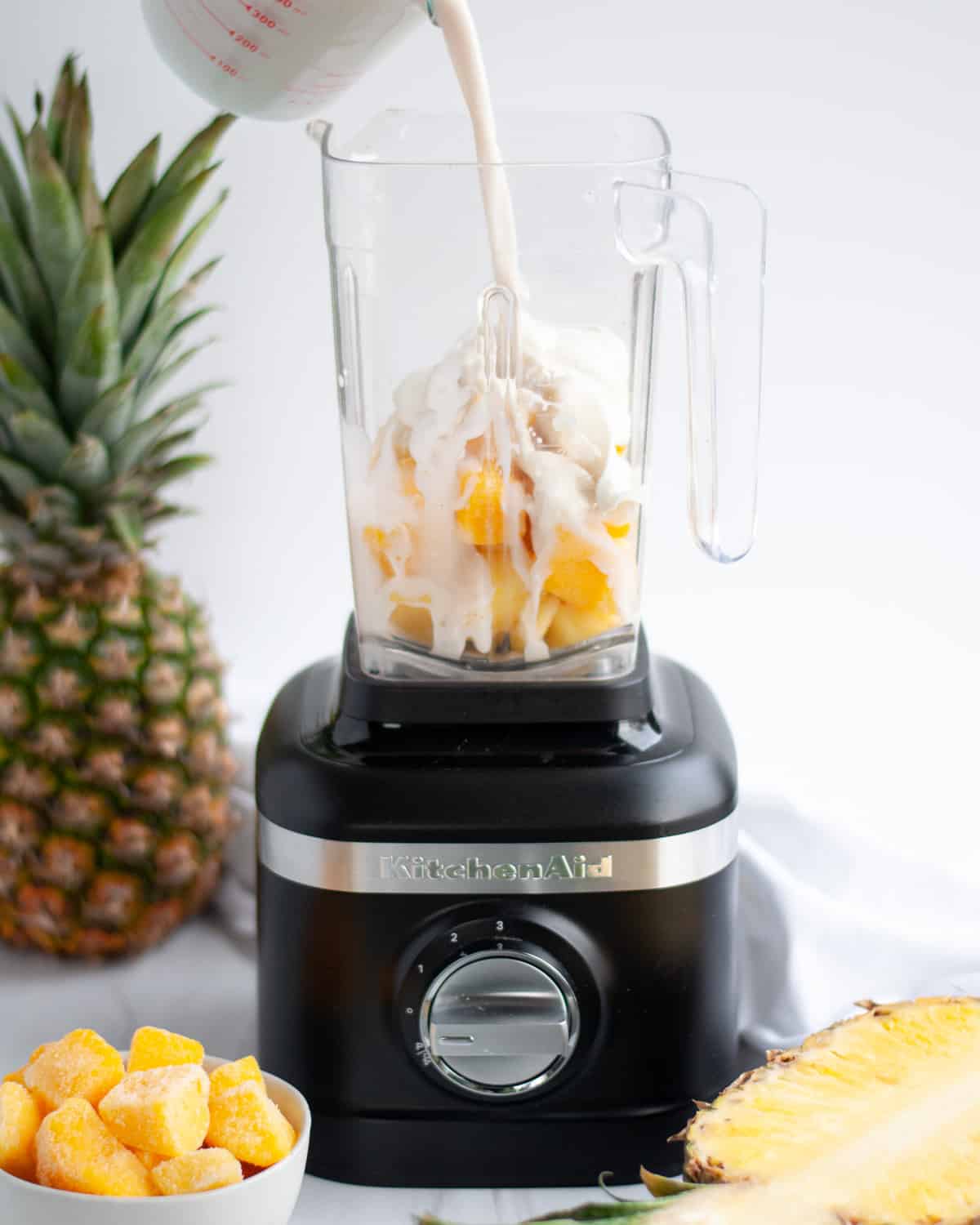 process shot showing how to make a mango pineapple smoothie, showing ingredients being added to a blender.