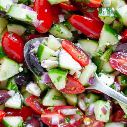 close up of a serving spoon filled with cucumber salad, sitting on top of more cucumber salad.