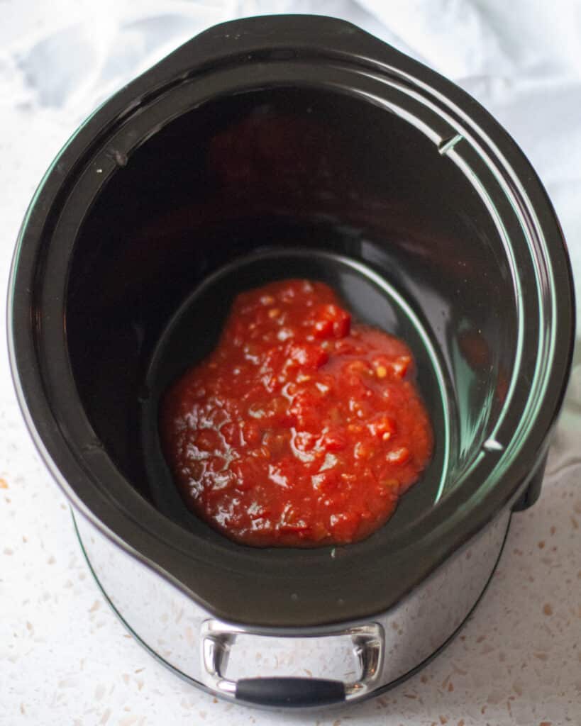 process shots showing how to make 2-ingredient crockpot salsa chicken. this image shows the first layer of salsa at the bottom of the crockpot.