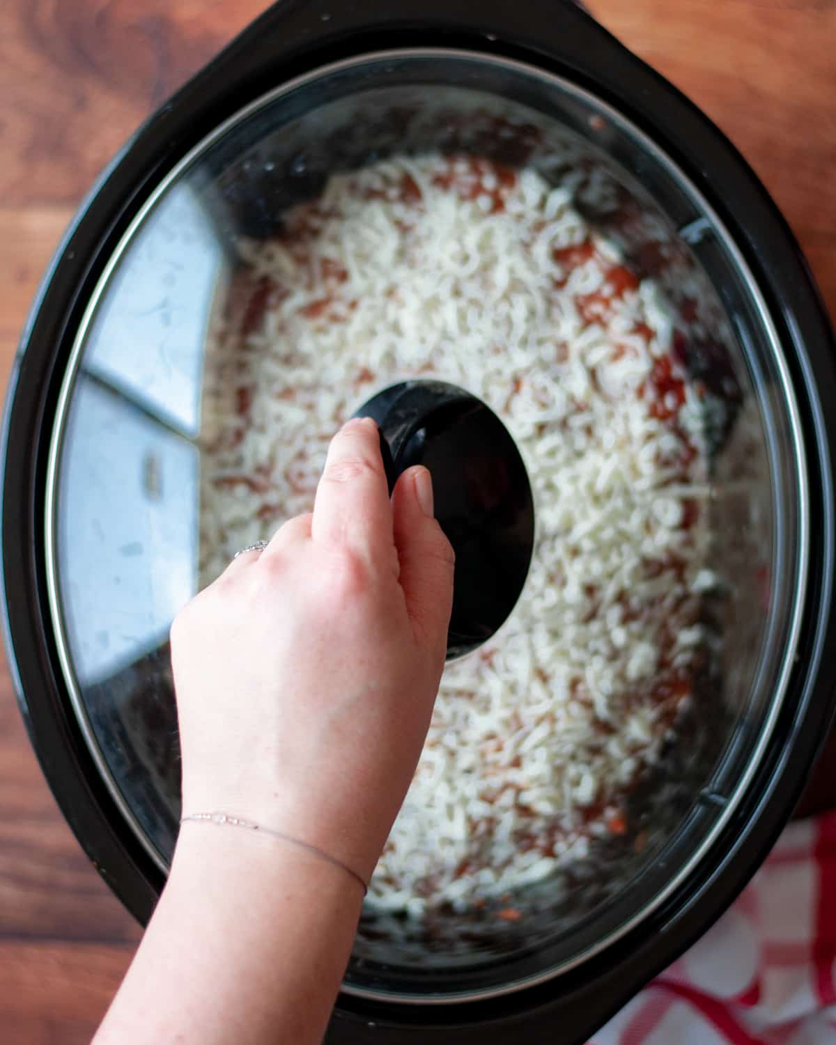 process shot showing how to make 4-ingredient crockpot ravioli. a hand is putting a cover on a crockpot, in anticipation of cooking.