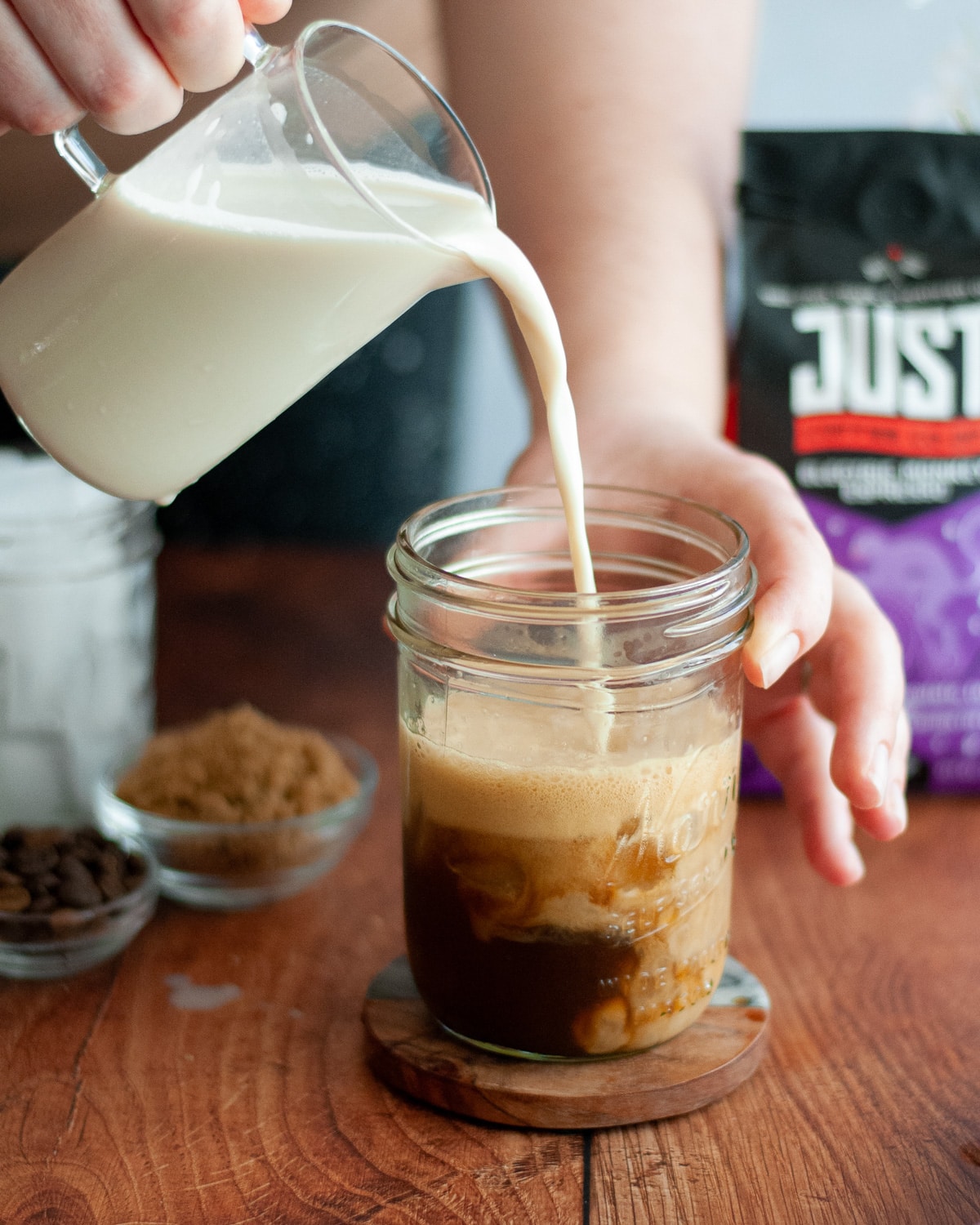 process shot for making a brown sugar shaken espresso: milk being poured into a jar of frothy, freshly shaken coffee.