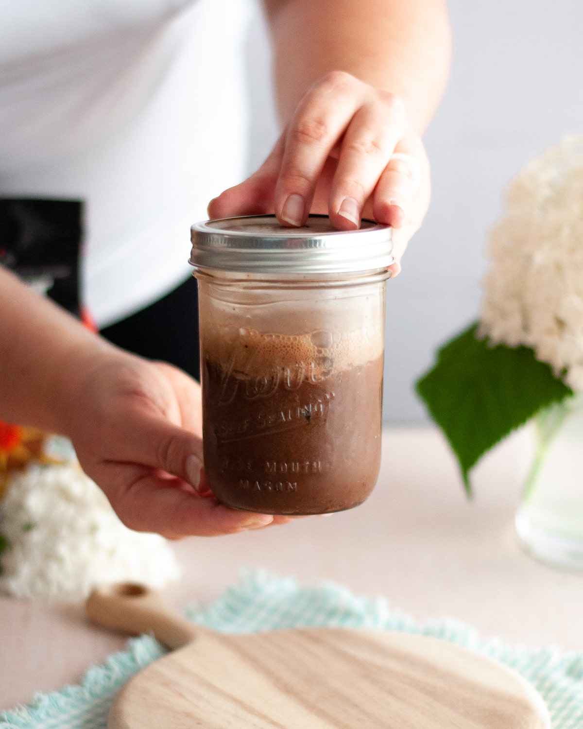 process shot showing how to make an iced chocolate almondmilk shaken espresso. here the chocolate malted milk powder, espresso, and ice are being shaken vigorously in a mason jar that is tightly sealed.
