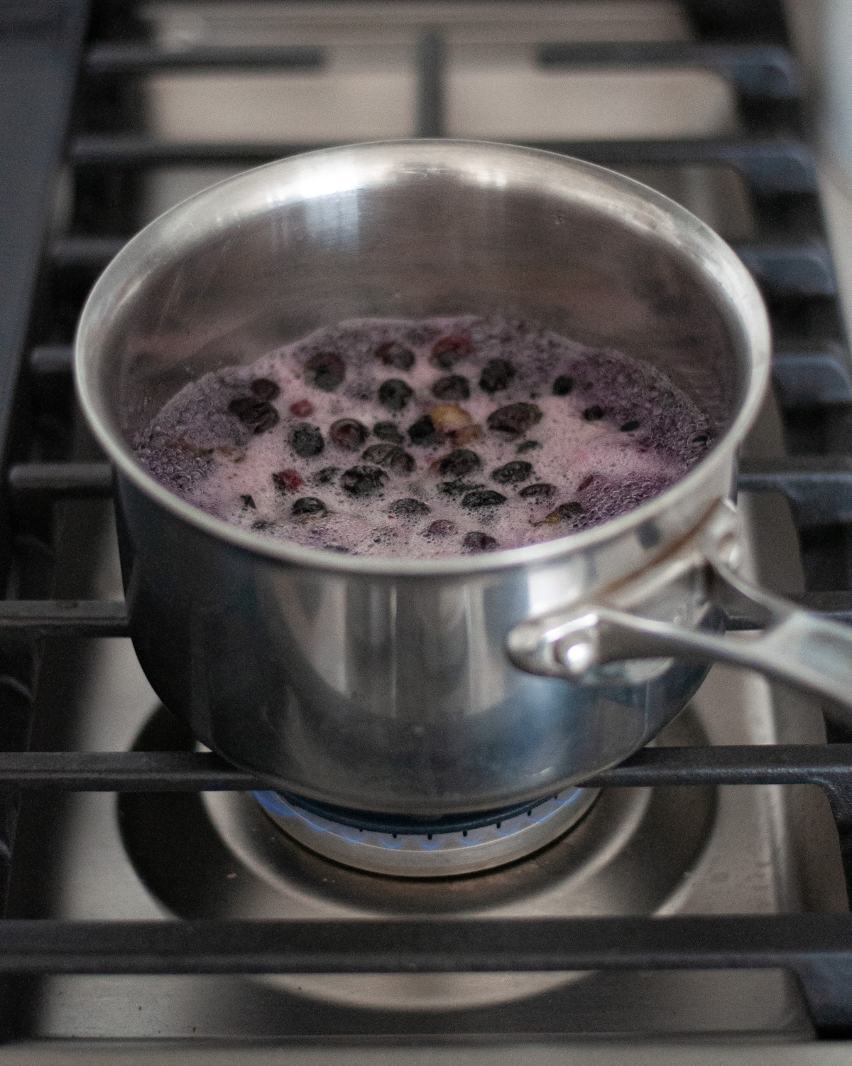 process shot for making blueberry simple syrup. this shot shows the water, sugar, and blueberries cooking over medium heat on the stove.