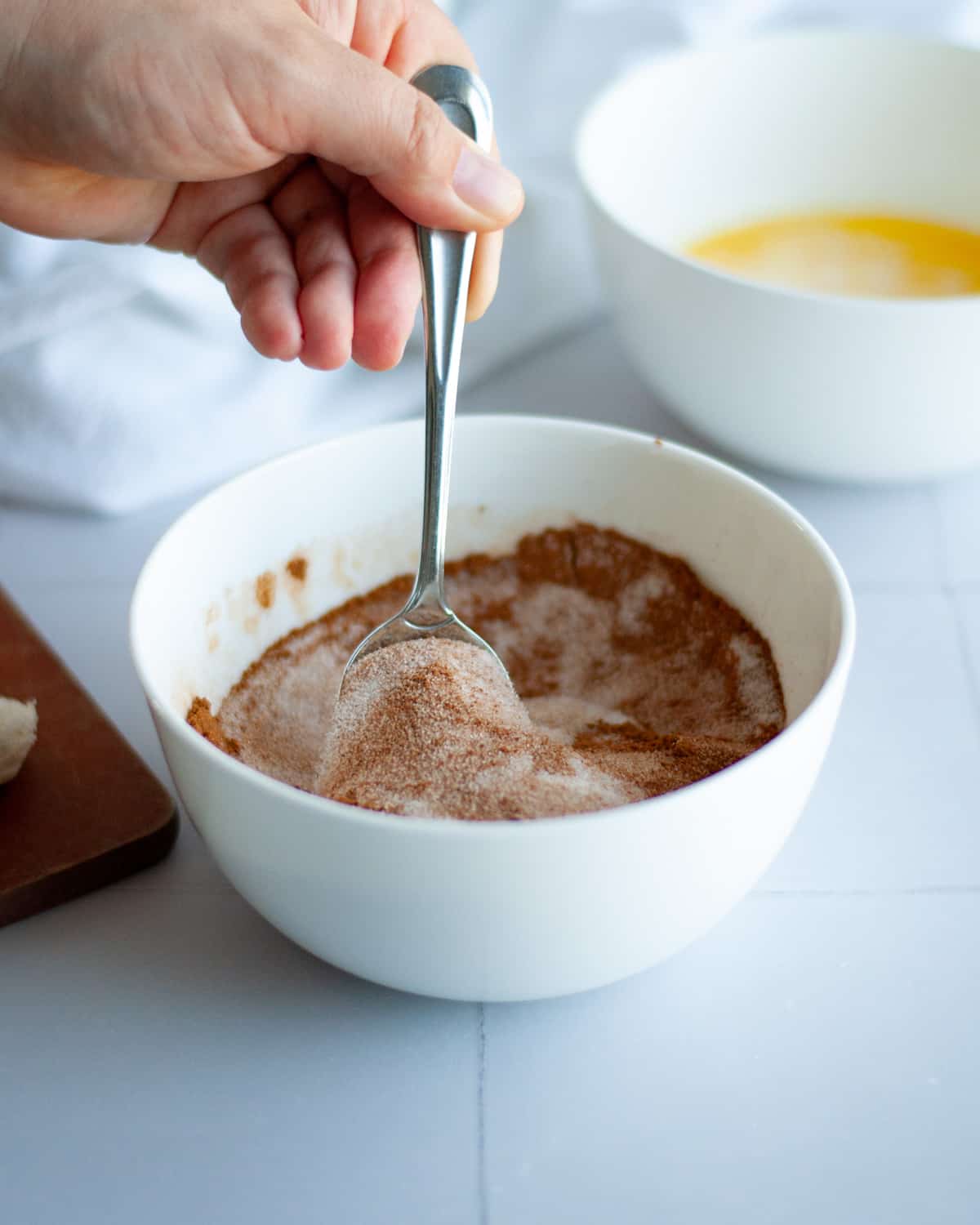 mixing together the cinnamon and sugar to dip the biscuit pieces into. a small bowl of melted butter sits in the background along with a white linen.